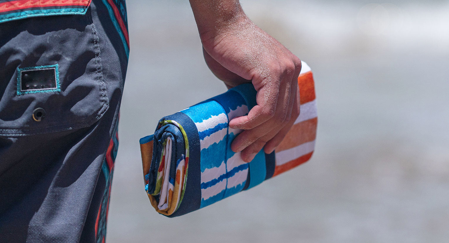 Person holding a rolled-up Lifeventure compact towel at the beach, ready for travel.