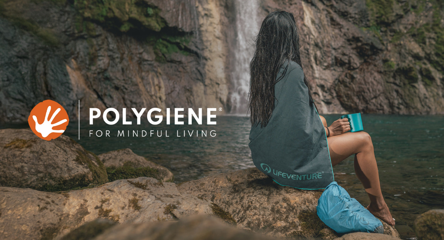 Woman sitting by a waterfall wrapped in a Lifeventure recycled towel with Polygiene technology.